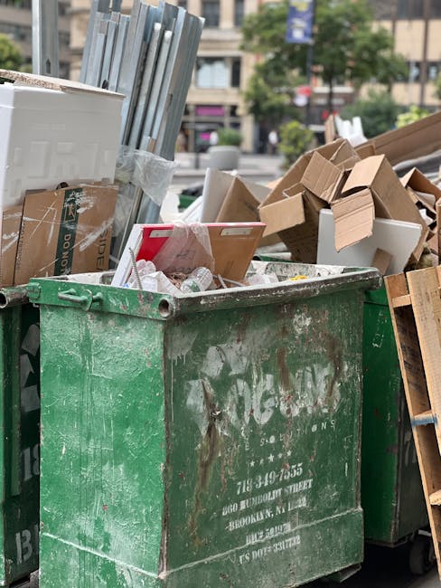 A black wheeled rubbish bin labeled 'St. John's' positioned on a sidewalk at night, filled with mixed waste including paper, cardboard, and plastic items, with some overflowing and protruding from the