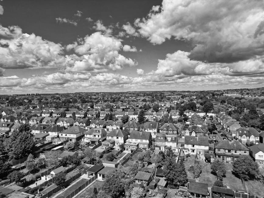 A black-and-white aerial photograph of a suburban residential area showing numerous detached and semi-detached houses with pitched roofs, surrounded by gardens and trees. The scene extends to the hori