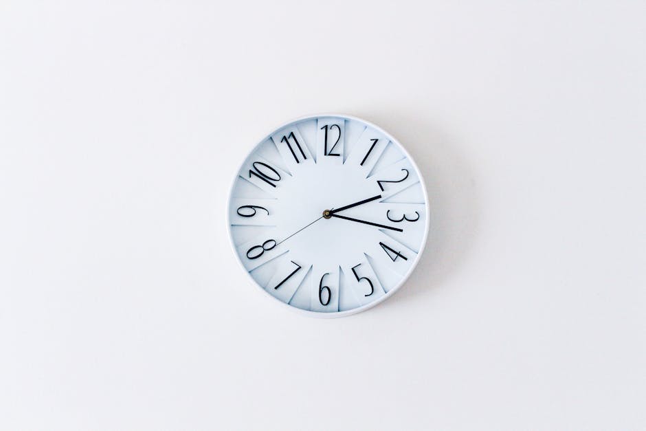 A modern round wall clock with a white face, black numerals, and black hour and minute hands shows approximately 2:13. The clock is mounted on a plain white wall, which appears clean and smooth, with no visible dust or smudges. The image emphasizes clear surface cleaning and maintenance, aligning with the focus on domestic cleaning and sanitization services offered by Cleaners Hounslow, as highlighted on the website page for same-day cleaning in Hounslow. The lighting is even, highlighting the minimalist and pristine appearance of the clock and wall, illustrating the importance of hygiene and upkeep in residential or commercial settings.